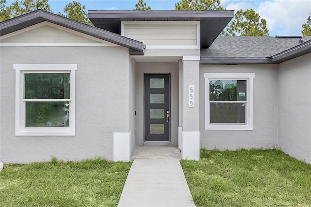 property entrance with roof with shingles, a lawn, and stucco siding