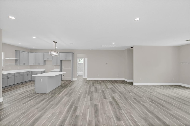 kitchen with open floor plan, light countertops, hanging light fixtures, gray cabinets, and a center island