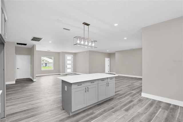 kitchen with a kitchen island, visible vents, open floor plan, light countertops, and decorative light fixtures