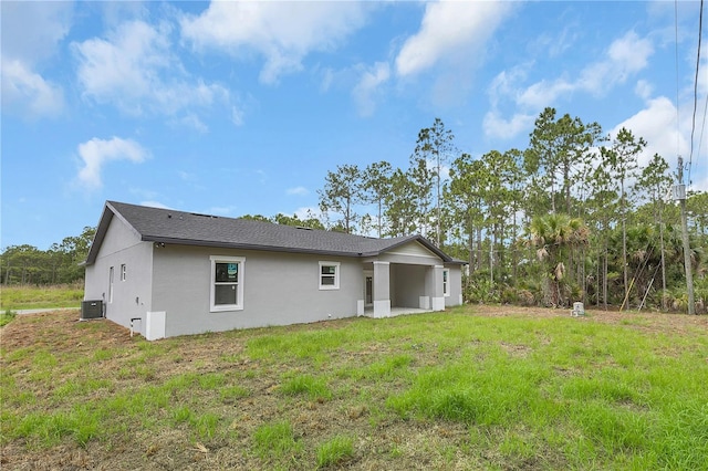 back of house featuring central AC, a lawn, and stucco siding