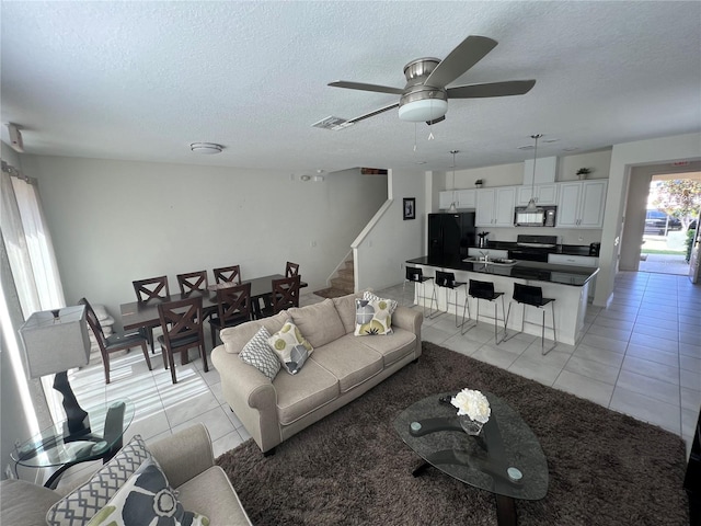 living room featuring ceiling fan, light tile patterned flooring, and a textured ceiling