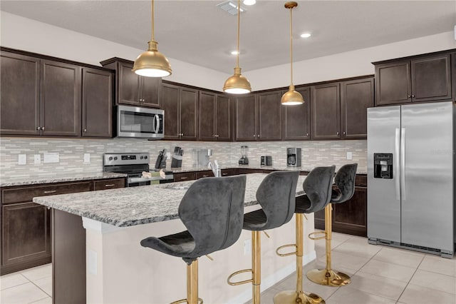 kitchen featuring light tile patterned flooring, appliances with stainless steel finishes, pendant lighting, and light stone counters