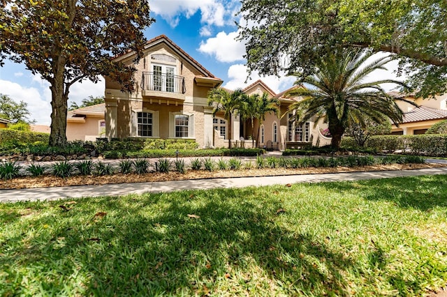 view of front of property featuring a balcony, a tile roof, a front lawn, and stucco siding