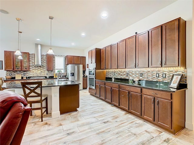 kitchen featuring pendant lighting, a kitchen breakfast bar, a center island, stainless steel appliances, and wall chimney range hood