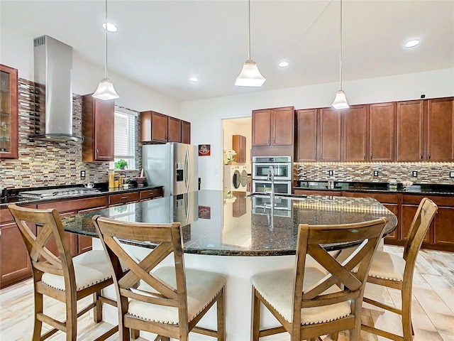 kitchen featuring a kitchen island, appliances with stainless steel finishes, wall chimney range hood, and decorative light fixtures