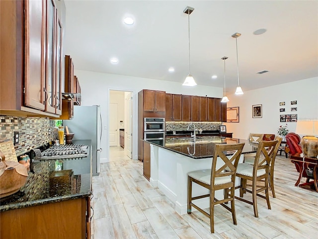 kitchen featuring decorative backsplash, dark stone counters, hanging light fixtures, and a center island with sink