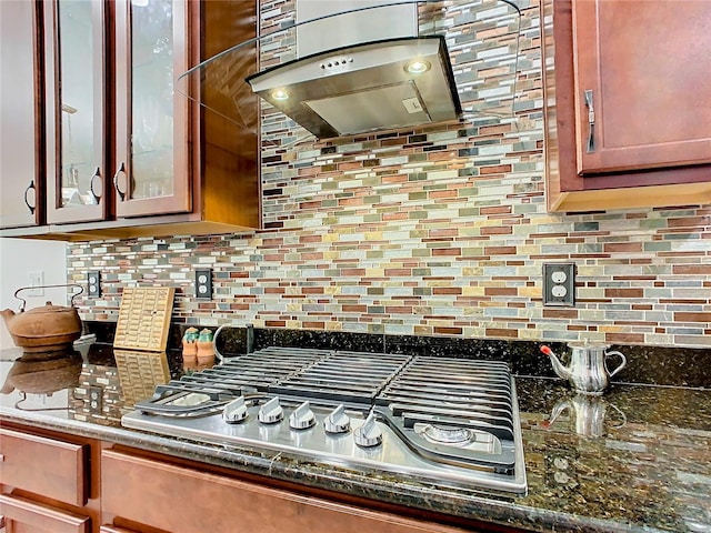 kitchen with island exhaust hood, dark stone counters, stainless steel gas cooktop, and backsplash