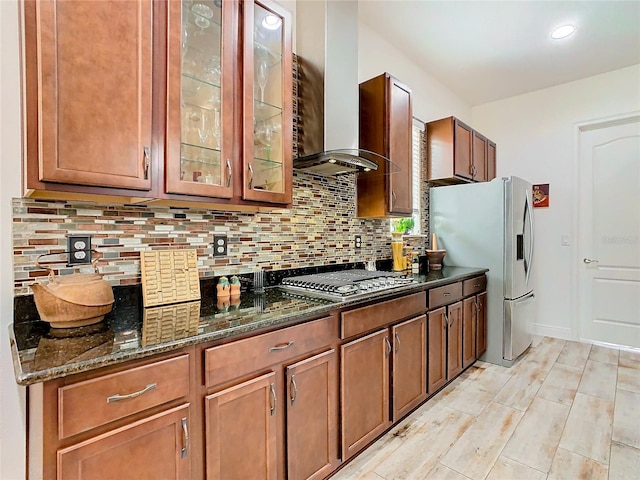 kitchen featuring appliances with stainless steel finishes, dark stone countertops, decorative backsplash, wall chimney range hood, and light wood-type flooring