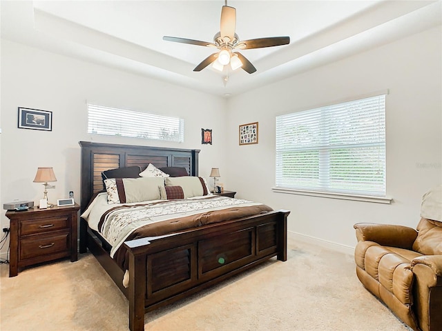 bedroom with a tray ceiling, light colored carpet, and ceiling fan