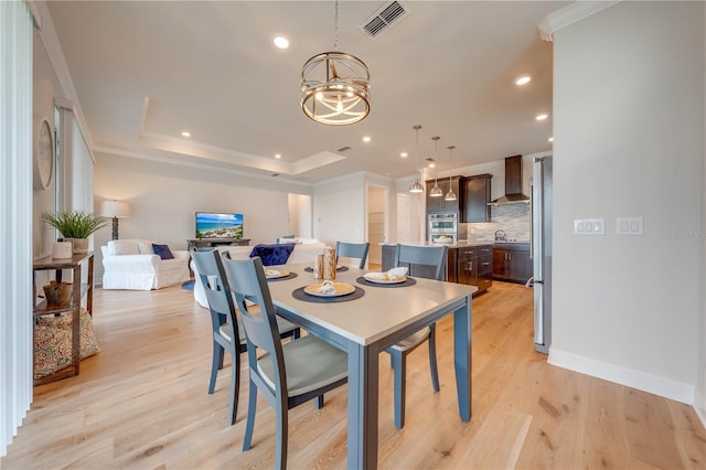 dining space with a tray ceiling, crown molding, sink, an inviting chandelier, and light hardwood / wood-style floors