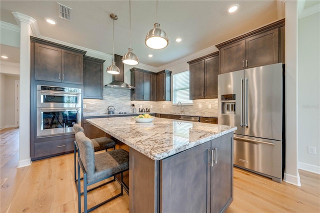 kitchen with dark brown cabinets, stainless steel appliances, wall chimney range hood, pendant lighting, and a center island