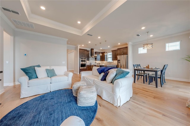 living room with a tray ceiling, crown molding, and light wood-type flooring