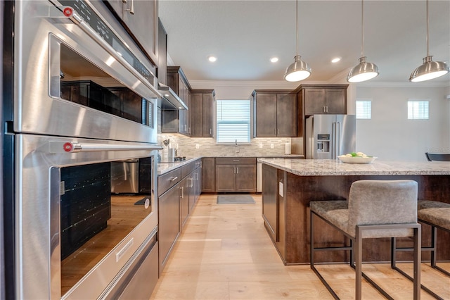 kitchen featuring a kitchen bar, pendant lighting, stainless steel appliances, and ornamental molding