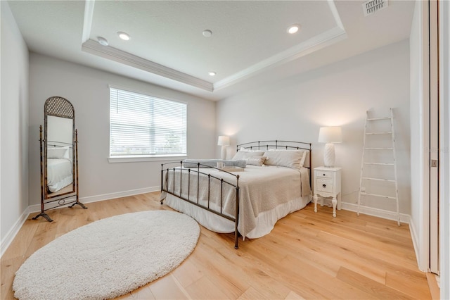 bedroom featuring light hardwood / wood-style floors, a raised ceiling, and crown molding