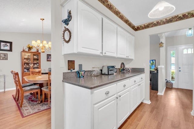 kitchen featuring vaulted ceiling, an inviting chandelier, white cabinets, light hardwood / wood-style floors, and hanging light fixtures