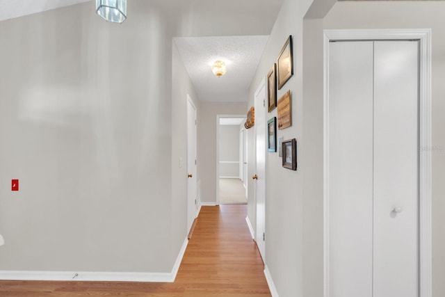 hallway with light hardwood / wood-style floors and a textured ceiling