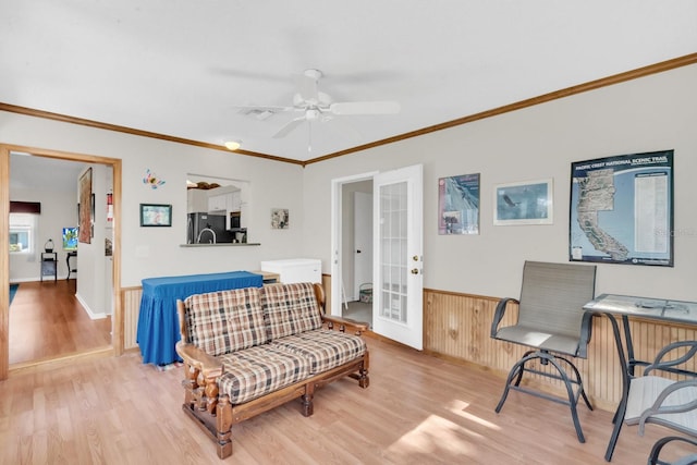 sitting room featuring wood walls, french doors, crown molding, light hardwood / wood-style flooring, and ceiling fan