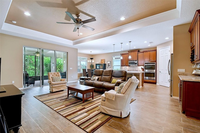 living room with a tray ceiling, ceiling fan, light hardwood / wood-style floors, and a textured ceiling