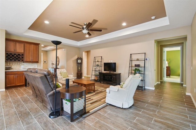 living room with ceiling fan, wood-type flooring, and a tray ceiling