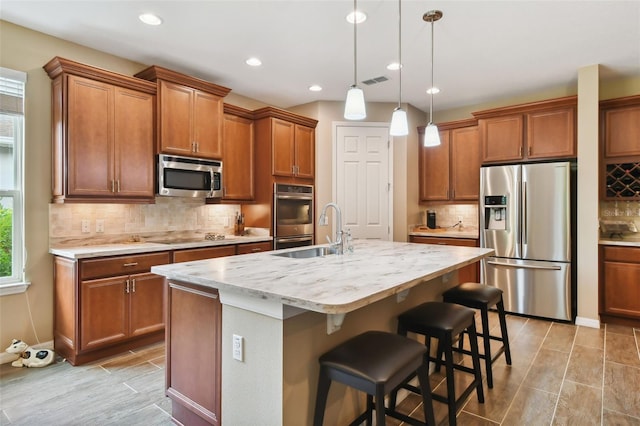 kitchen with appliances with stainless steel finishes, a breakfast bar, a kitchen island with sink, sink, and hanging light fixtures