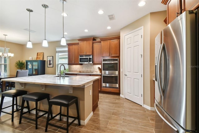 kitchen featuring sink, decorative light fixtures, a kitchen island with sink, a breakfast bar, and appliances with stainless steel finishes