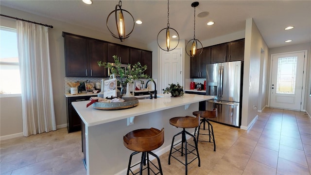 kitchen with a kitchen breakfast bar, hanging light fixtures, stainless steel fridge, an island with sink, and tasteful backsplash