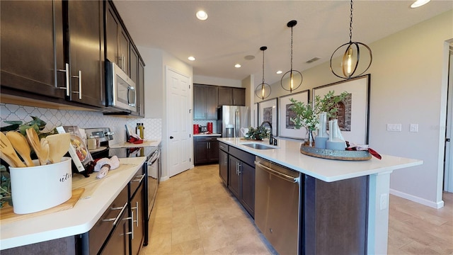 kitchen with a center island with sink, sink, hanging light fixtures, tasteful backsplash, and stainless steel appliances