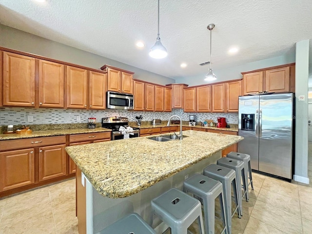 kitchen featuring sink, stainless steel appliances, pendant lighting, a kitchen bar, and a center island with sink