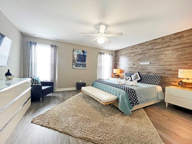 bedroom featuring a textured ceiling, hardwood / wood-style flooring, ceiling fan, and wood walls