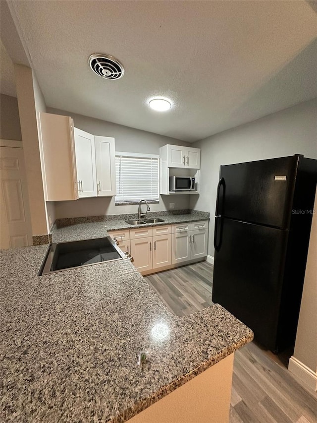 kitchen featuring black fridge, kitchen peninsula, sink, a textured ceiling, and white cabinetry