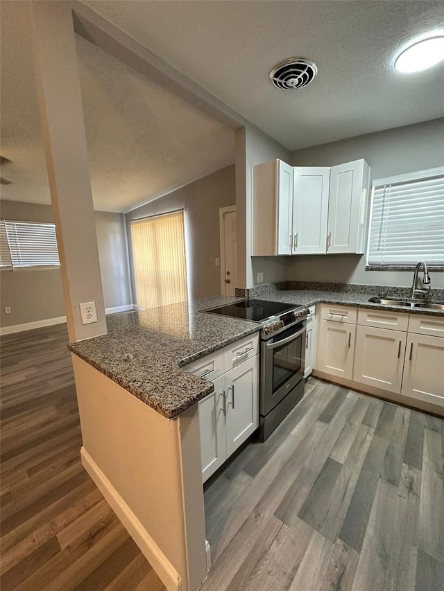 kitchen featuring kitchen peninsula, sink, electric range, dark stone countertops, and white cabinetry