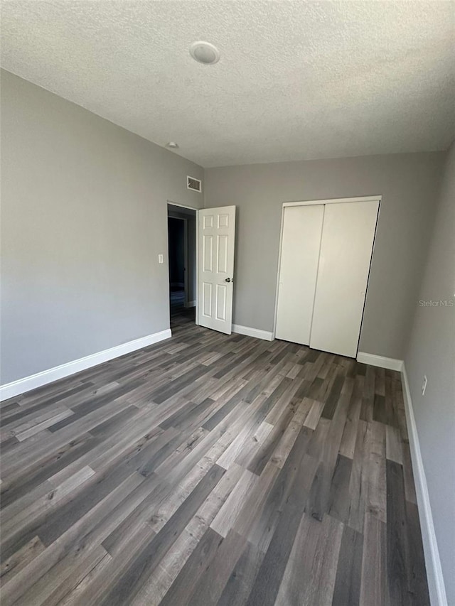 unfurnished bedroom featuring a textured ceiling, a closet, and dark hardwood / wood-style floors