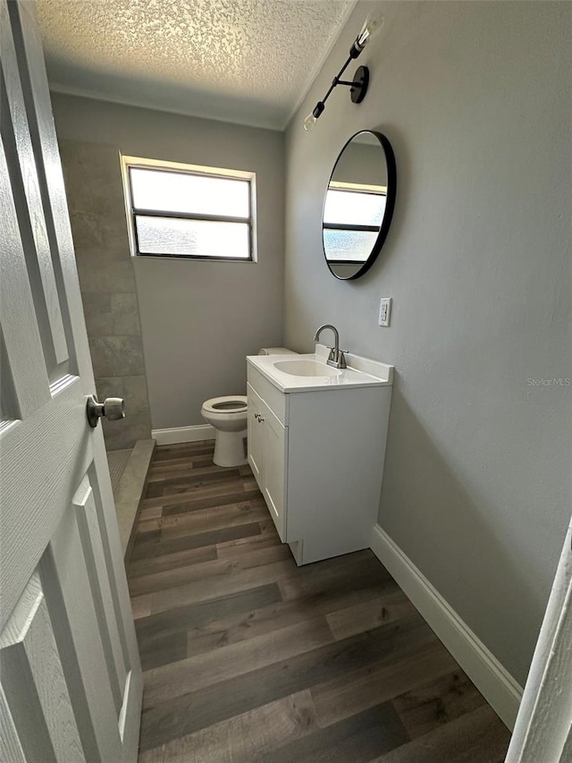 bathroom featuring walk in shower, vanity, a textured ceiling, hardwood / wood-style flooring, and toilet