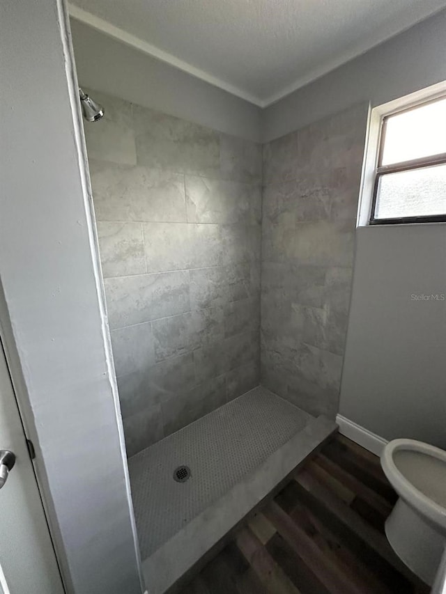 bathroom with tiled shower, hardwood / wood-style flooring, and toilet