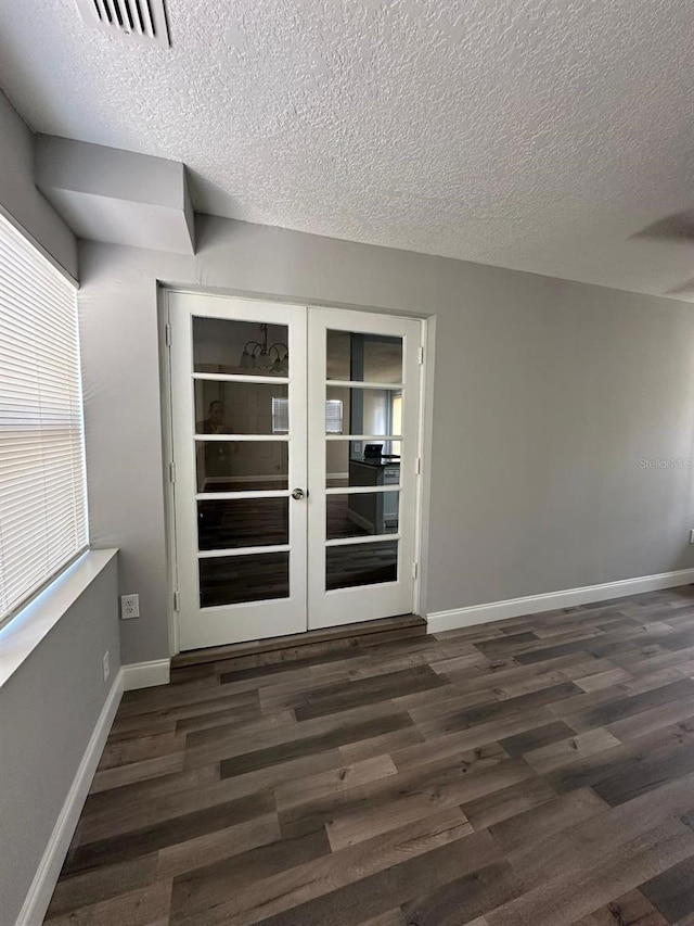 empty room with plenty of natural light, french doors, a textured ceiling, and dark wood-type flooring