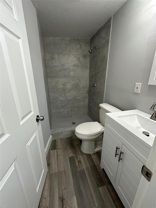 bathroom with a tile shower, hardwood / wood-style floors, a textured ceiling, toilet, and vanity