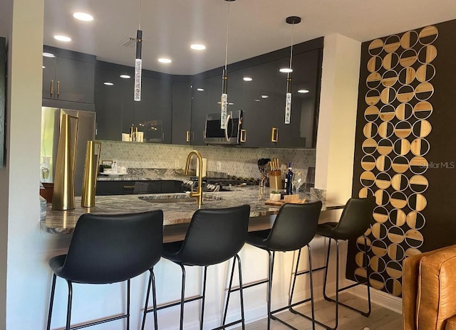 kitchen featuring appliances with stainless steel finishes, kitchen peninsula, sink, light hardwood / wood-style flooring, and decorative light fixtures