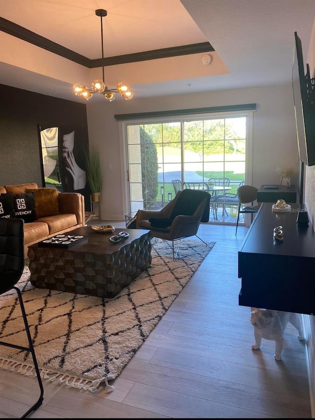 living room with wood-type flooring, a raised ceiling, a healthy amount of sunlight, and a notable chandelier