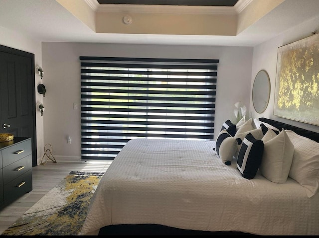 bedroom with crown molding, light wood-type flooring, and a raised ceiling