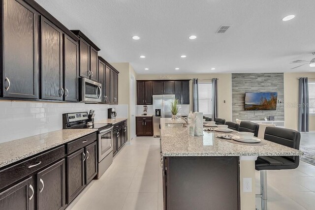 kitchen featuring dark brown cabinetry, stainless steel appliances, tasteful backsplash, an island with sink, and a breakfast bar area