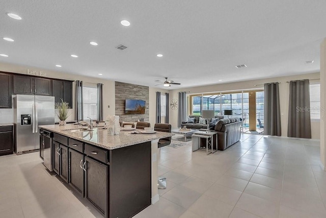 kitchen featuring light stone countertops, black dishwasher, an island with sink, sink, and stainless steel fridge