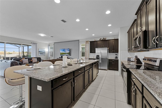 kitchen featuring an island with sink, sink, backsplash, stainless steel appliances, and a breakfast bar area