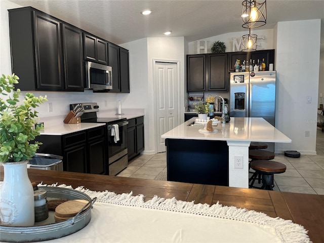 kitchen with appliances with stainless steel finishes, a kitchen island with sink, pendant lighting, sink, and light tile floors