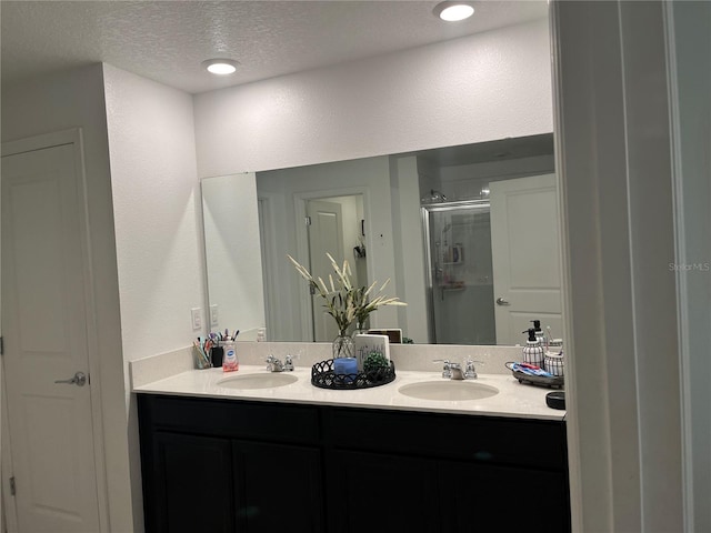 bathroom featuring double vanity, an enclosed shower, and a textured ceiling