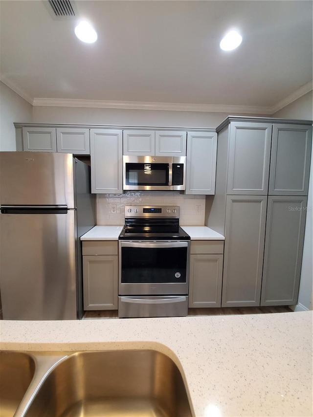 kitchen with tasteful backsplash, crown molding, gray cabinets, and appliances with stainless steel finishes