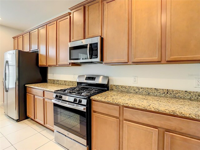 kitchen with appliances with stainless steel finishes, light stone countertops, and light tile floors