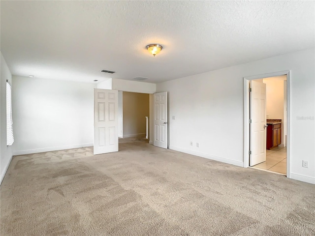 unfurnished bedroom featuring light carpet, ensuite bath, and a textured ceiling