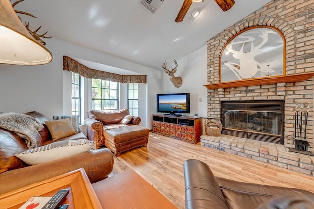 living room with wood finished floors, visible vents, a ceiling fan, vaulted ceiling, and a brick fireplace