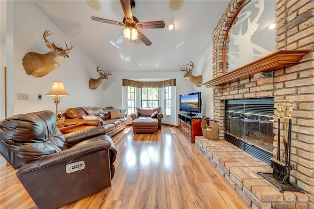 living room featuring hardwood / wood-style floors, ceiling fan, lofted ceiling, and a brick fireplace