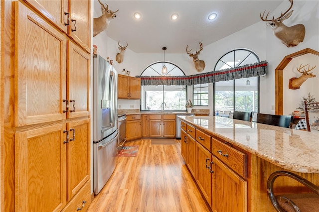 kitchen featuring light wood-style flooring, appliances with stainless steel finishes, brown cabinets, a breakfast bar, and a sink